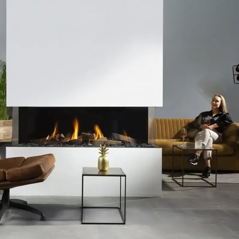 Element4 Summum 140 3S, en moderne gasspeis med tre glassflater, integrert i en hvit vegg. Flammene danser over naturtro keramiske vedkubber og en LED-belyst glødende bunn, omgitt av minimalistiske møbler i nøytrale toner og en grønn plante som tilfører kontrast
