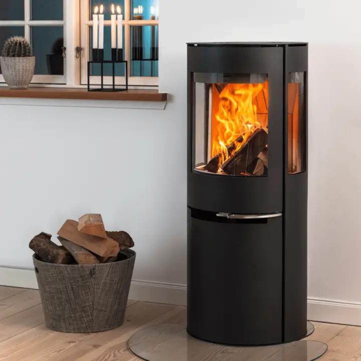 Aduro hybrid kombinert ved- & pelletsovn bilde – moderne sort sylindrisk hybridovn med koselige flammer i lys stue hos Peisbutikken.no