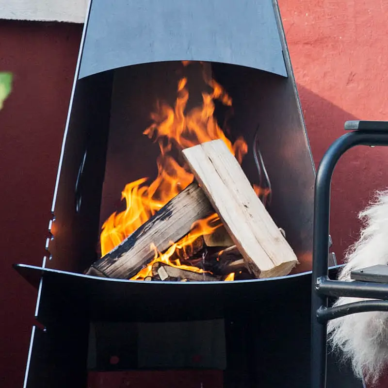 Aduro utepeis sort Corten livsstilsbilde – moderne sort Corten stål utepeis med koselige flammer og ved i bruk på terrasse hos Peisbutikken.no
