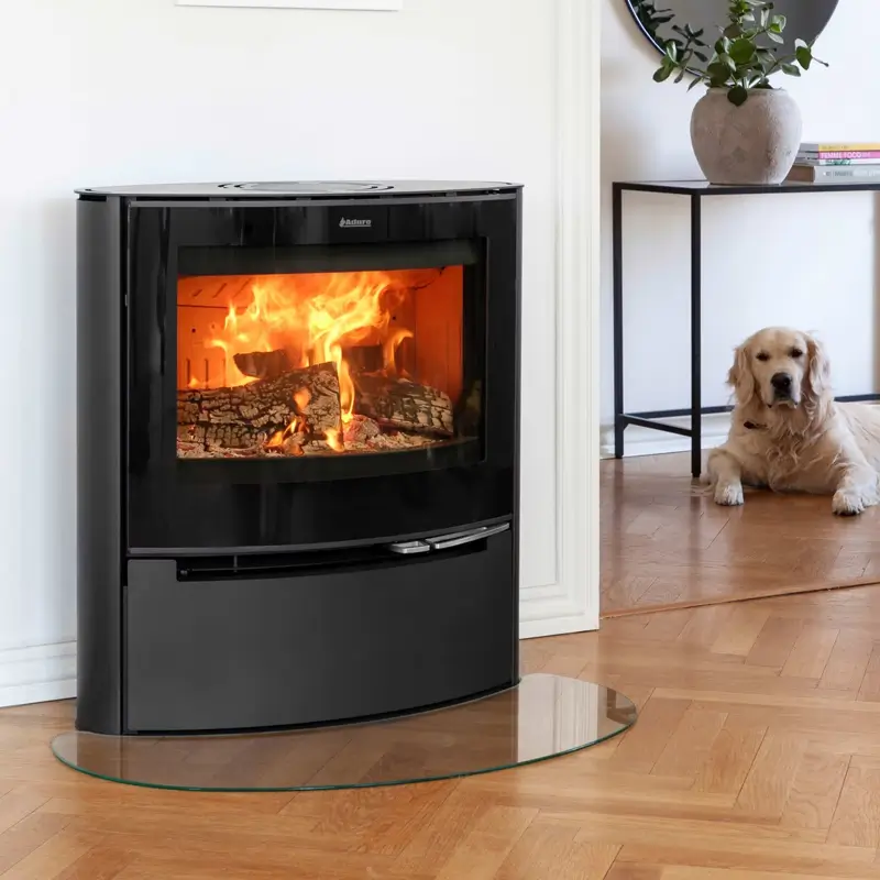 Aduro 15 Lux Peisovn livsstilsbilde – moderne sort buet vedovn med panoramiske flammer i lys skandinavisk stue med golden retriever og glassplate hos Peisbutikken.no