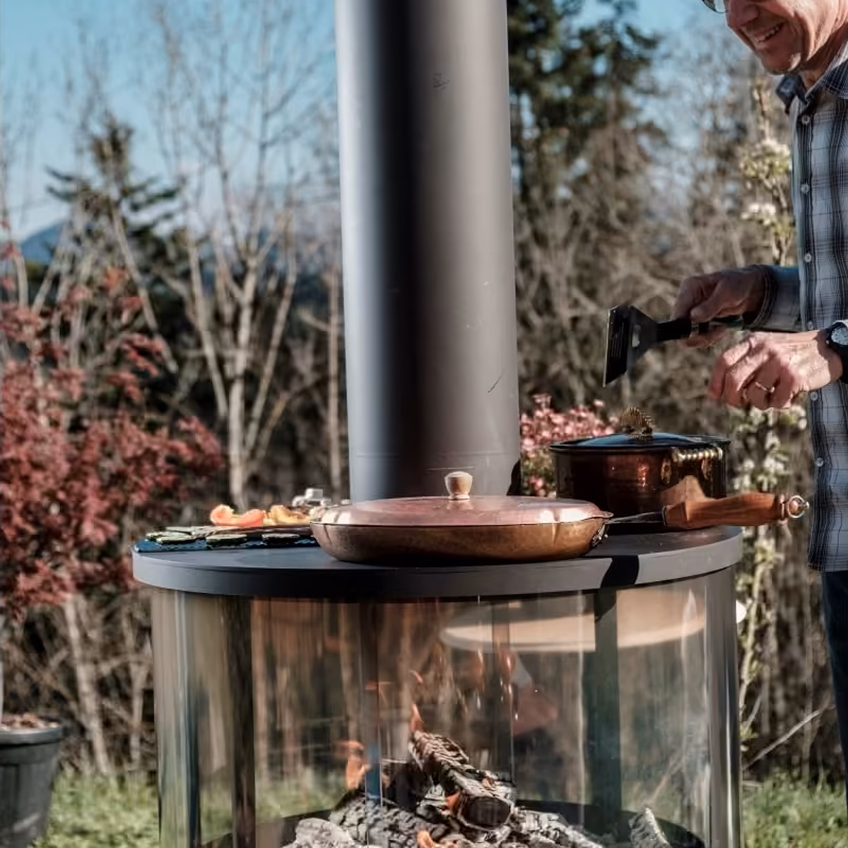 Rüegg Surprise utepeis – mann lager mat på den moderne sorte ovnen med panoramaglass og ferske grønnsaker i solrik hage hos Peisbutikken.no