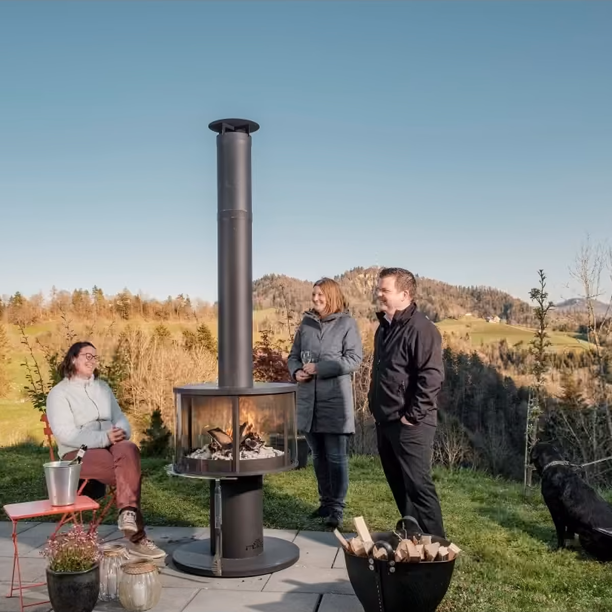 Rüegg Surprise utepeis – gruppe venner slapper av rundt panoramiske flammer i vakker hage hos Peisbutikken.no