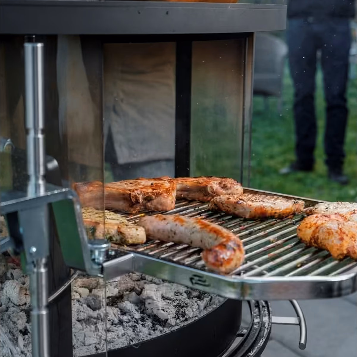 Rüegg Surprise utepeis – nærbilde av grilling pølser og kjøtt på svingbar grill med glødende kull hos Peisbutikken.no