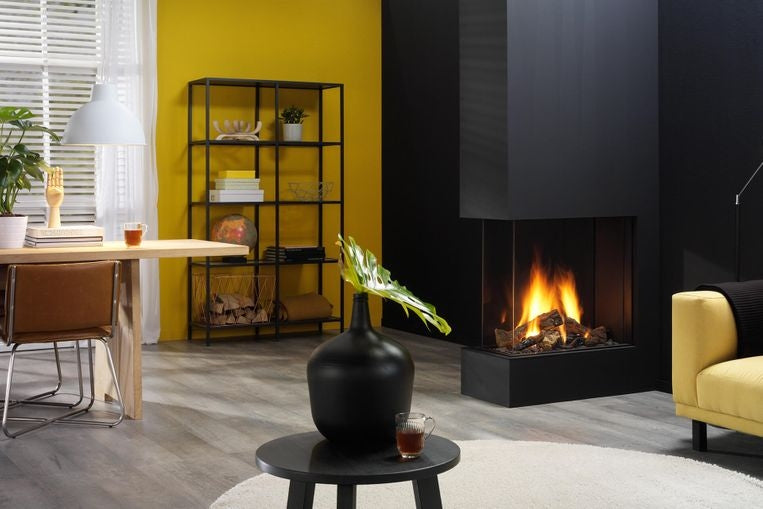 Trimline 73 H Romdeler livsstilsbilde – bred moderne innebygd lineær gasspeis brukt som elegant romdeler med realistiske dansende flammer i lys åpen stue med gul accentvegg, svart pipe, koselig sofa og planter hos peisbutikken.no