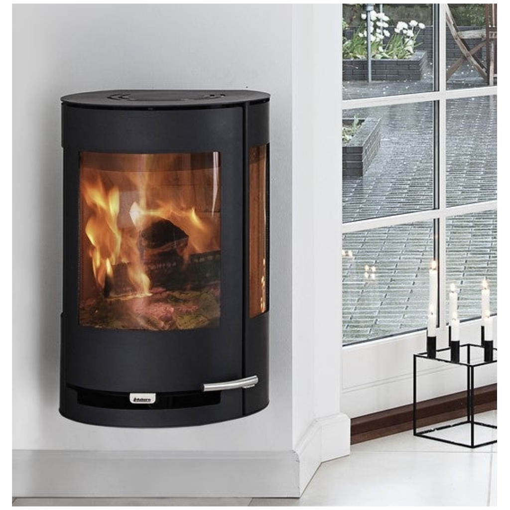 Aduro 9.4 Wall livsstilsbilde – moderne svart veggmontert hjørne vedovn med stort buet panoramaglass og levende realistiske flammer, montert høyt på hvit vegg i lys samtids stue med store vinduer, hageutsikt, tregulv og mykt naturlig lys hos peisbutikken.no