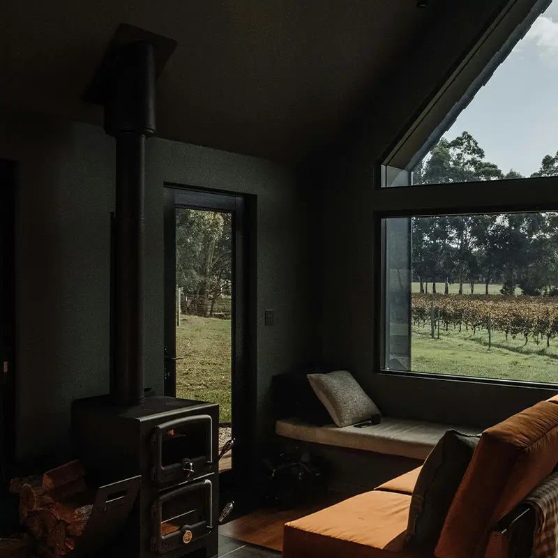 Stålpipe Universal blogg bilde – sort universelt pipeløp montert på moderne sort vedovn i koselig mørk stue med vinmarksutsikt hos Peisbutikken.no