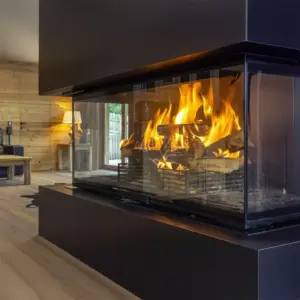 Rüegg RIII 45×56×46 er en tre-sidig peisinnsats plassert i en trepanelt stue, der panoramaglass gir bred innsikt til flammene og skaper et lunt og iøynefallende midtpunkt i rommet