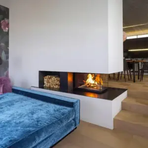 Rüegg RIII 55×56×46 tre-sidig peisinnsats elegant integrert mellom stue og spiseområde, med bred flammeutsikt fra flere vinkler og tilknytning til en tretrapp som tilfører varme og arkitektonisk karakter til det åpne rommet.