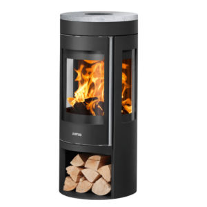 Justus Mino Trios 2.0 Kleberstein vedfyrt peisovn på hvit bakgrunn med sideglassvisninger, vedlager, topp røykrørtilkobling og aktive flammer, som fremhever klebersteinbelegg for peis-oppvarming.