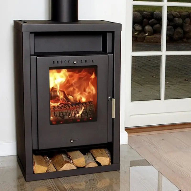 Asgard 2 sort rektangulær peisovn plassert innendørs nær en hvit vegg og stort vindu med utsikt over en utendørs steinvegg og hage, med en flat topp med røykrør, øvre ventilert panel, sentralt glassvindu som viser lyse oransje flammer og brennende vedkubber i brannkammeret, et sølv dørhåndtak til høyre, et nedre askerom med knapp, og en åpen basesokkel som holder stablede vedkubber, og understreker dens høye boksete struktur, solide kanter og praktiske lagring i et tregulvet rom for vedfyrt oppvarming.