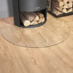 Justus/Oranier stor glassgulvplate til runde ovner – elegant klar herdet glassbeskyttelse under sort ovn i koselig stue hos Peisbutikken.no