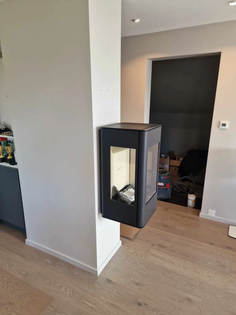 Veggmontert peis under montering i moderne stue med svart ramme, emballasje og verktøy rundt – profesjonell peismontering av sertifiserte montører fra Peisbutikken.no