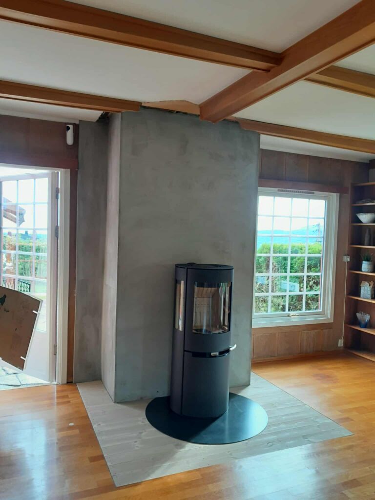 Aduro vedovn profesjonelt montert av Peisbutikken i Enebakk – moderne sort ovn med panoramaglass på rund gulvplate mot betongvegg